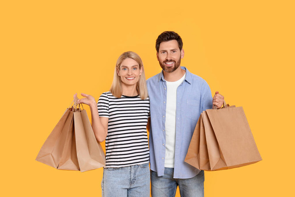 Family shopping. Happy couple with paper bags on orange background - Fotografie, Obrázek