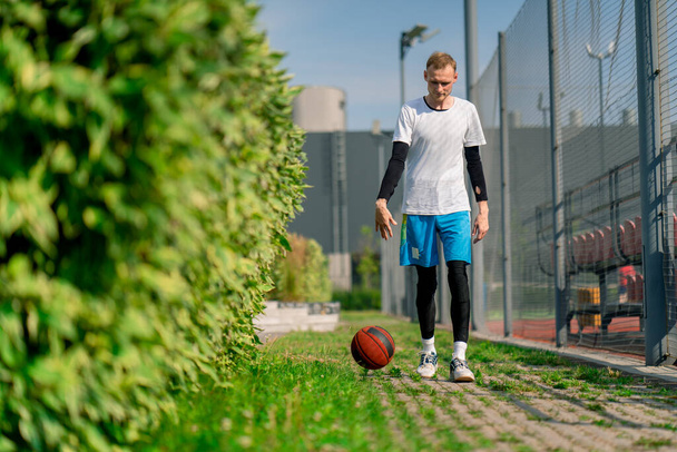 背の高い男のバスケットボールプレーヤーは,バスケットボールコートへの公園の道を歩いて,彼のドリブルスキルを披露するボールを駆動します - 写真・画像