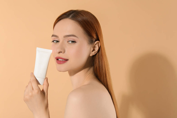 Beautiful young woman holding sun protection cream on beige background, space for text - Fotografie, Obrázek