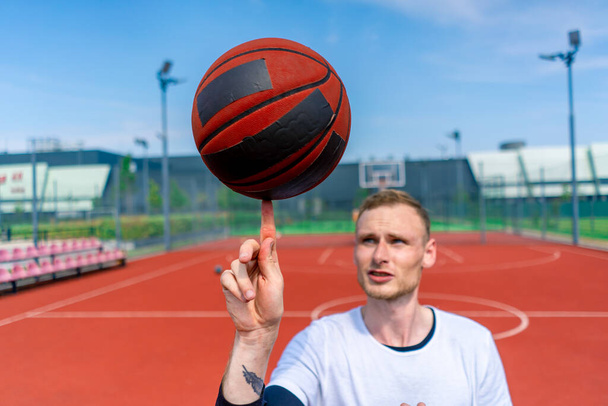 彼のバスケットボールのフリースタイルスキルを示す彼の指にバスケットボールを回転する男のバスケットボール選手のクローズアップ - 写真・画像