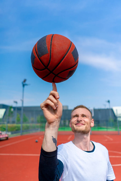 Крупный план парня-баскетболиста, вращающего баскетбольный мяч на пальце, демонстрирующего свои навыки вольного стиля - Фото, изображение