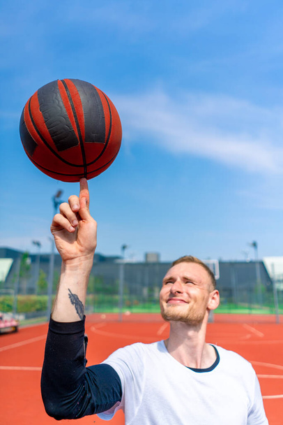 Крупный план парня-баскетболиста, вращающего баскетбольный мяч на пальце, демонстрирующего свои навыки вольного стиля - Фото, изображение