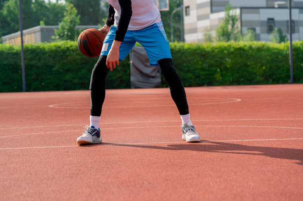 Magas srác kosaras a labdával mutatja a csöpögő képességeit edzés közben a parkban a kosárpályán. - Fotó, kép