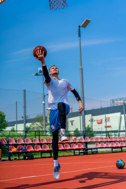 Großer Basketballspieler springt mit dem Ball in der Hand zum Korb, um beim Training auf dem Basketballplatz im Park einen spektakulären Dunk zu erzielen - Foto, Bild