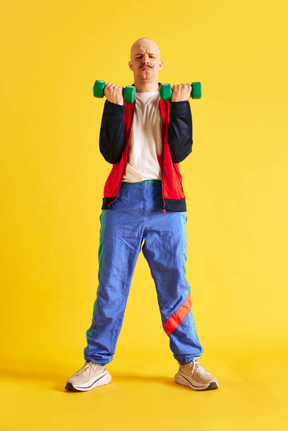 Вид спереди. Полное изображение тела молодого спортсмена, одетого в спортивную одежду и делающего упражнения с ярко-зелеными манекенами на жёлтом фоне. Концепция спорта, здорового образа жизни, тренировок и рекламы - Фото, изображение