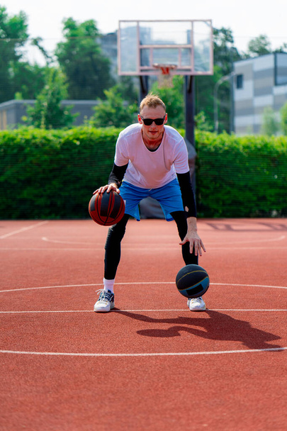 2つのボールを持つ背の高い男のバスケットボール選手は,公園のバスケットボールコートで練習しながら,彼のドリブルスキルを披露します - 写真・画像