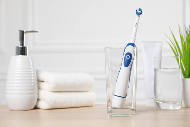 Electric toothbrush, glass of water and toiletries on wooden table - Фото, изображение
