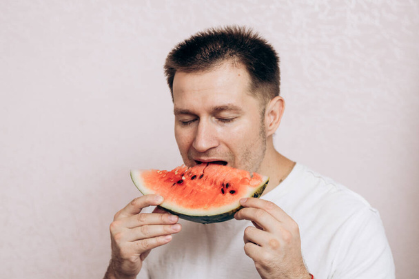 Хлопець у білій футболці тримає стиглий кавун і їсть його. Літні фрукти з саду - Фото, зображення