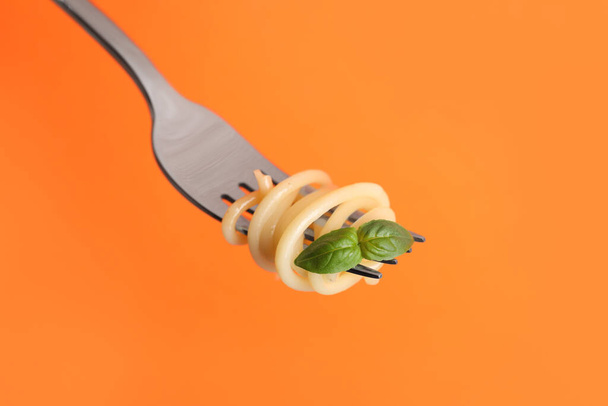 Fork with tasty pasta and basil on orange background, closeup - Foto, afbeelding