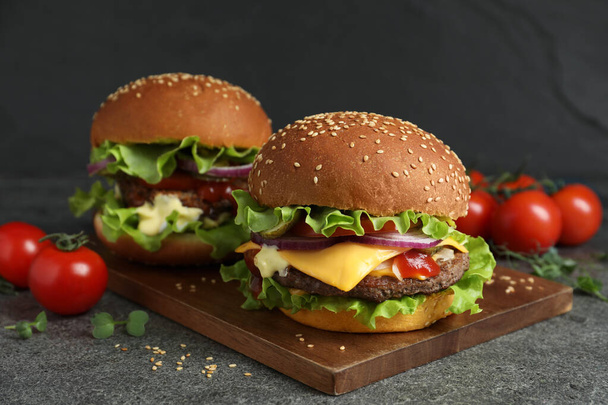 Delicious burgers with beef patty and tomatoes on grey table - Fotoğraf, Görsel