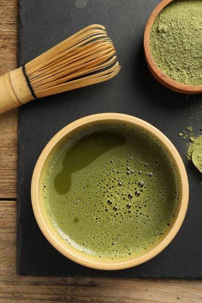 Cup of fresh matcha tea, green powder and bamboo whisk on wooden table, top view - Фото, зображення
