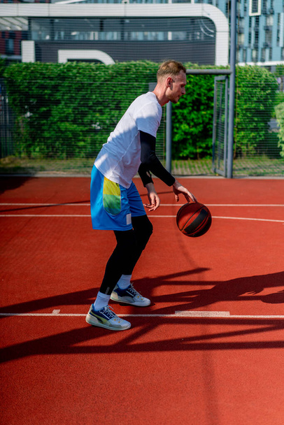Großer Basketballspieler mit dem Ball zeigt seine Dribbelkünste beim Training auf dem Basketballplatz im Park - Foto, Bild