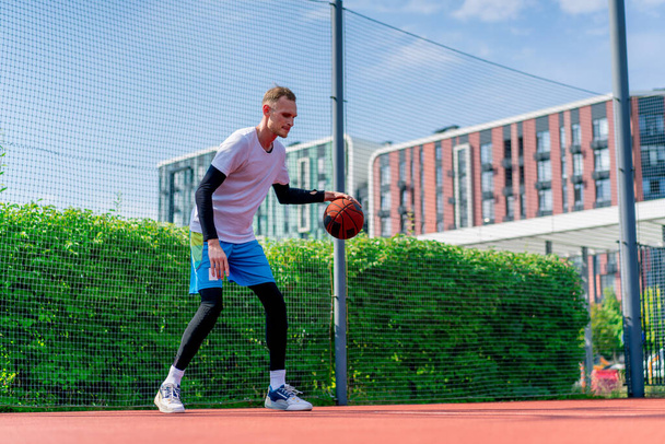 Grand joueur de basket-ball avec la balle montre ses compétences dribble pendant l'entraînement sur le terrain de basket-ball dans le parc - Photo, image