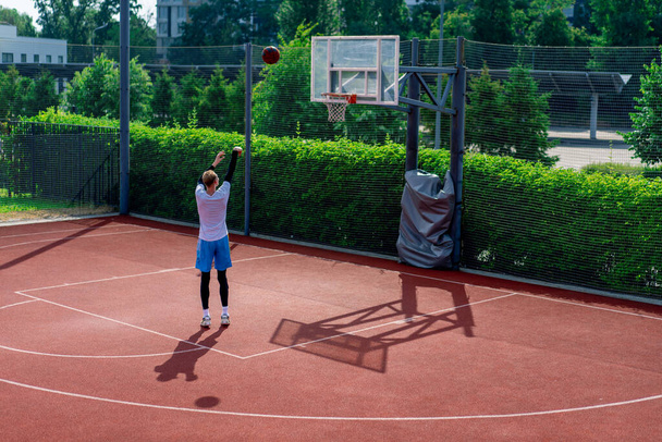 jogador de basquete cara alto lança uma bola em um aro de basquete em uma quadra de basquete no parque durante o treino - Foto, Imagem