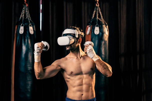 Boxer εκπαίδευση χρησιμοποιώντας την τεχνολογία VR ή εικονική πραγματικότητα, φορώντας ακουστικά VR με καθηλωτική τεχνική προπόνηση πυγμαχίας χρησιμοποιώντας ελεγκτή για να ενισχύσει τις ικανότητές του στο περιβάλλον προσομοιωτή πυγμαχίας. Ιμπέτους - Φωτογραφία, εικόνα