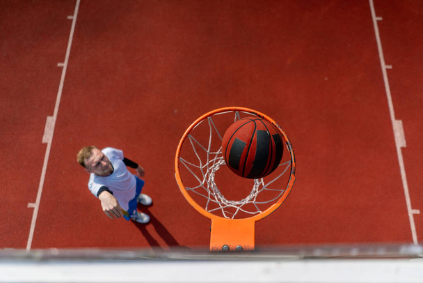 Primer plano del anillo de baloncesto en el que un jugador de baloncesto de hombre alto lanza la pelota desde abajo el concepto de admirar el juego de baloncesto - Foto, imagen