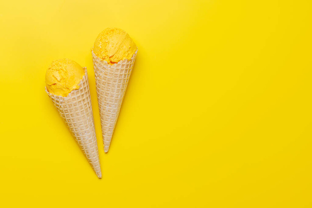 Helado de limón en deliciosos conos de gofres, una delicia para todos los gustos. Sobre fondo amarillo con espacio de copia, plano - Foto, Imagen