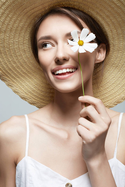 cheerful village girl in hat with flower. beautiful smiling young woman with chamomile - Fotografie, Obrázek
