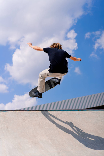 A young guy skater does a stunt on the edge of a skatepool against a backdrop of sky and clouds at city skate park - Foto, afbeelding