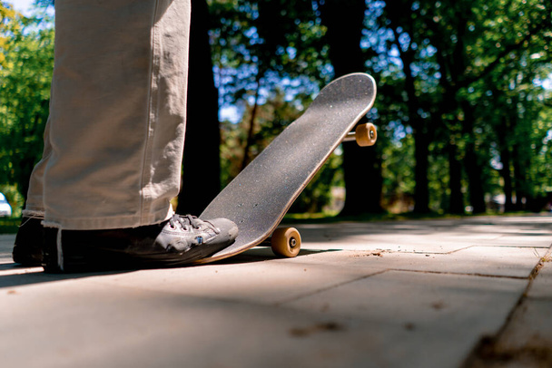 νεαρός πατινέρ βόλτες skateboard στο μονοπάτι του πάρκου της πόλης με φόντο τα δέντρα και τον ουρανό γκρο πλαν - Φωτογραφία, εικόνα