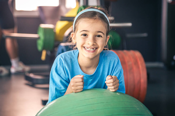 Glückliches Mädchen dehnt ihren Körper auf einem Fitball in der Turnhalle, Turnen und Pilates für Kinder. - Foto, Bild