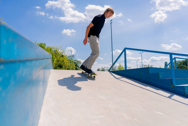 Молодой скейтбордист скейтбординг по городу скейтпарк рядом с фигурами для трюков - Фото, изображение