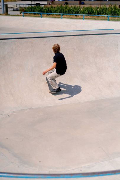 Jovem skatista cara com skate de cabelo longo e fazendo truques na piscina de skate no parque de skate da cidade - Foto, Imagem