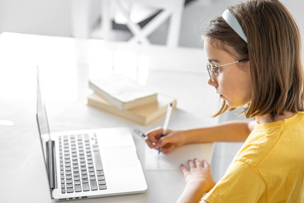 Una adolescente haciendo tarea sentada con libros y portátil, concepto de aprendizaje en línea, niño estudiando en casa. - Foto, imagen