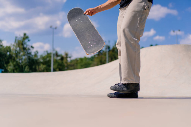 Close-up Een jonge skateboarder gooit een skateboard met zijn handen en probeert een stunt te doen in het skatepark van de stad - Foto, afbeelding