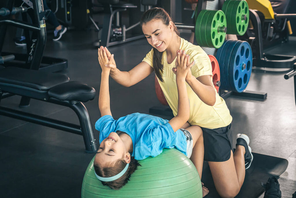 Little sportowa dziewczyna i młoda piękna matka robi rozciąganie z piłką fitness na siłowni. - Zdjęcie, obraz