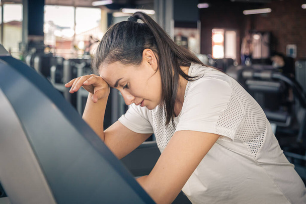A young woman on treadmill in gym, tired girl on a racetrack at the gym. - Photo, Image