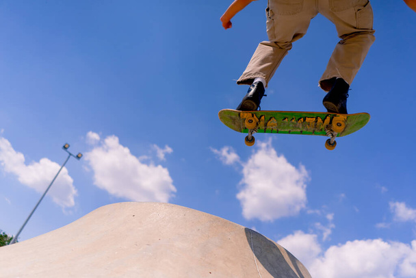 Mladý kluk bruslař dělá kaskadérský kousek na okraji skatepoolu na pozadí oblohy a mraky v městském skate parku - Fotografie, Obrázek