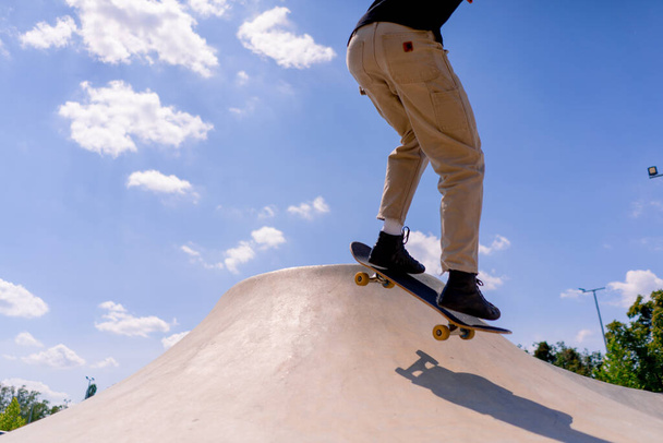 Молодой парень-фигурист делает трюк на краю скейтпола на фоне неба и облаков в городском скейт-парке - Фото, изображение