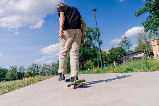молодой парень катается на скейтборде по тропе городского парка на фоне деревьев и неба - Фото, изображение