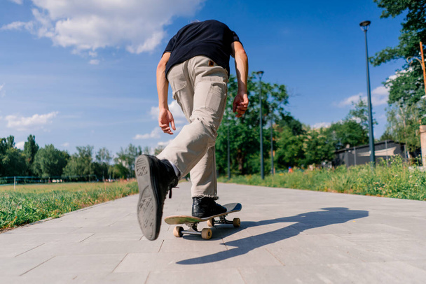 молодий хлопець катається на скейтборді на шляху міського парку на тлі дерев і неба - Фото, зображення