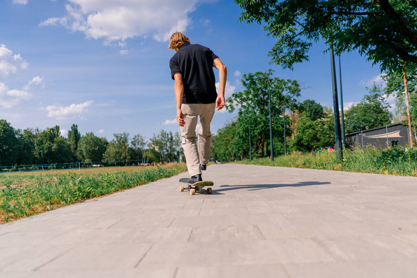 若い男スケーターは,木や空の背景に対して,市立公園のパスにスケートボードに乗ります - 写真・画像