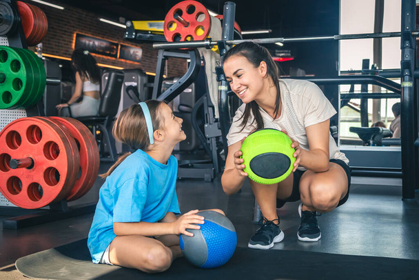 Strong mother with daughter in the gym go in for sports, use balls, happy family. - Photo, Image
