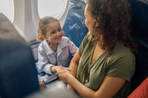飛行機に座っている少女の高い角度のビューでは、彼女の母親に笑みを浮かべている間、一緒に旅行している。家族、休暇の概念 - 写真・画像