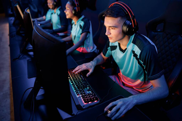 Młody gracz esports koncentruje się na grze nosząc przewodowy zestaw słuchawkowy podczas gry online multiplayer w klubie cybernetycznym - Zdjęcie, obraz