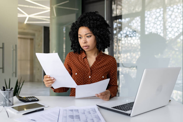 Sad disappointed businesswoman inside office at workplace looking at documents papers financial reports, african american female worker on paper work depressed unhappy with financial achievements - 写真・画像