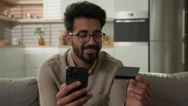 Χαμογελαστός χαρούμενος Αραβικός Ινδός πελάτης πελάτης πελάτης αρσενικός καταναλωτής τύπος ψώνια σε απευθείας σύνδεση με χρήση τηλεφώνου πιστωτική κάρτα mobile bank app αγοράζουν τρόφιμα παράδοση στο σπίτι κουζίνα πληρώνουν χρήματα για την υπηρεσία e-banking - Πλάνα, βίντεο