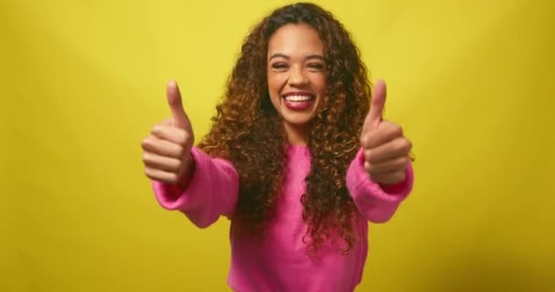 Gyönyörű többnemzetiségű nő ad dupla hüvelykujj fel, sárga stúdió háttér. Kiváló minőségű 4k felvételek - Felvétel, videó