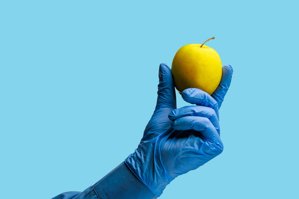 Uma maçã na mão do médico. Antecedentes com foco seletivo. Cenário médico azul isolado - Foto, Imagem