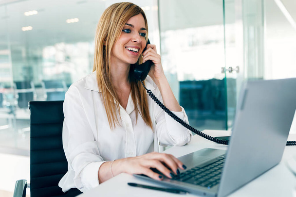 Shot of elegant attractive businesswoman talking with telephone while working with laptop in a modern startup - Foto, imagen
