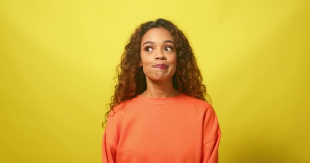 Cute young woman pulls funny faces, nervous and shy, yellow studio background. High quality 4k footage - Footage, Video