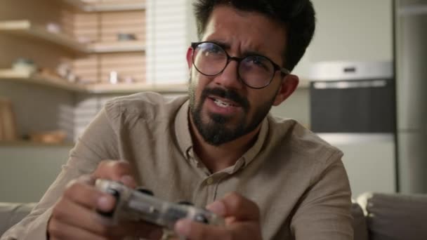 Indiai arab férfi etnikai srác érezd jól magad kanapén játék online video játék intelligens TV konzol virtuális vezetés autó használata vezeték nélküli vezérlő szórakozás otthon konyha férfi játékos játszik joystick - Felvétel, videó