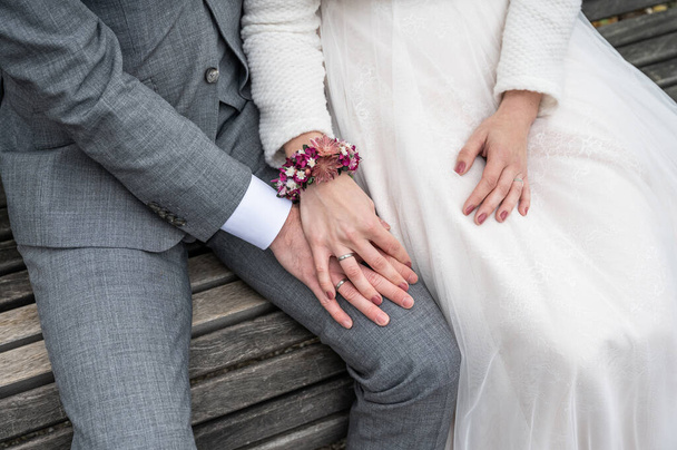 Bride holding groom hand with wedding rings sitting on bench. - Zdjęcie, obraz
