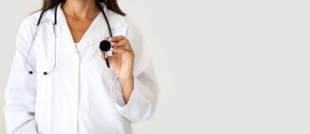 Європейська жінка середнього віку лікар дієтолог у білому пальто використовує стетоскоп, слухає дихання, ізольований на світлому фоні студії, панораму. Професійний іспит та охорона здоров'я, лікування - Фото, зображення
