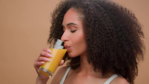 Όμορφη ευτυχισμένη υγιή αφρο-αμερικανική γυναίκα έθνικ κορίτσι θηλυκό μοντέλο με σγουρά μαλλιά πίνοντας φρέσκο χυμό πορτοκαλιού βιταμίνη ποτό διατροφή detox βιολογική χορτοφάγος υγειονομική περίθαλψη χαμογελώντας στο στούντιο φόντο - Πλάνα, βίντεο