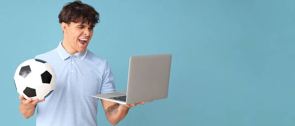 Huutava nuori mies, jolla on jalkapallo ja kannettava tietokone sinisellä taustalla, jossa on tilaa tekstille - Valokuva, kuva